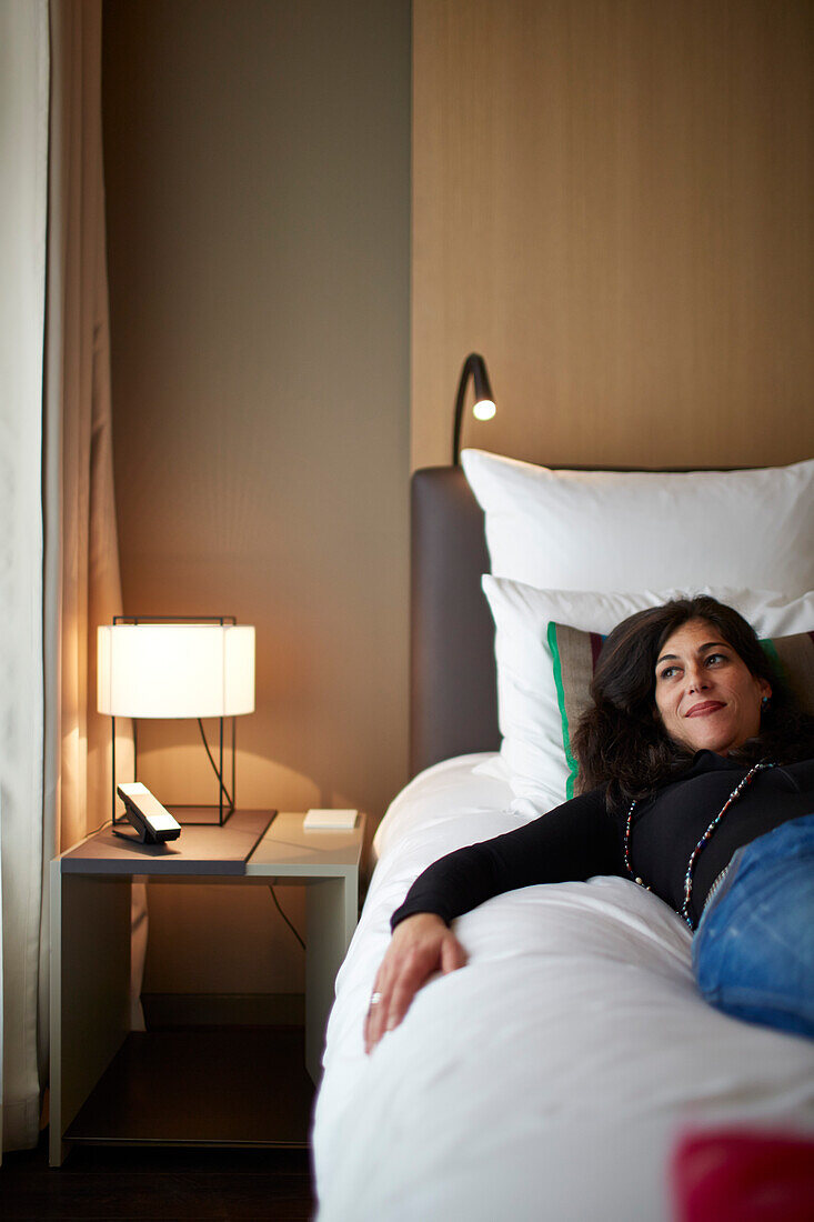 Woman lying on the bed in a standard room, Das Stue Hotel, Drakestrasse 1, Tiergarten, Berlin, Germany
