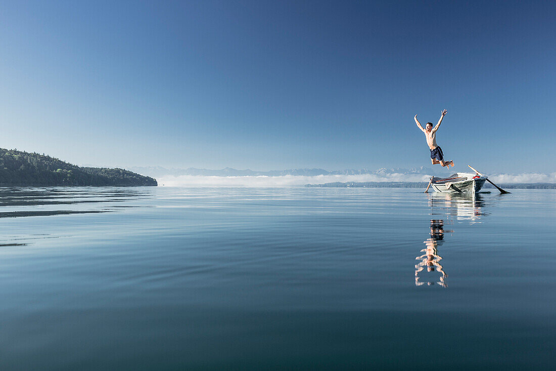 Man swimming in lake Starnberg, the Alps with mount Zugspitze in early morning fog, Berg, Upper Bavaria, Germany