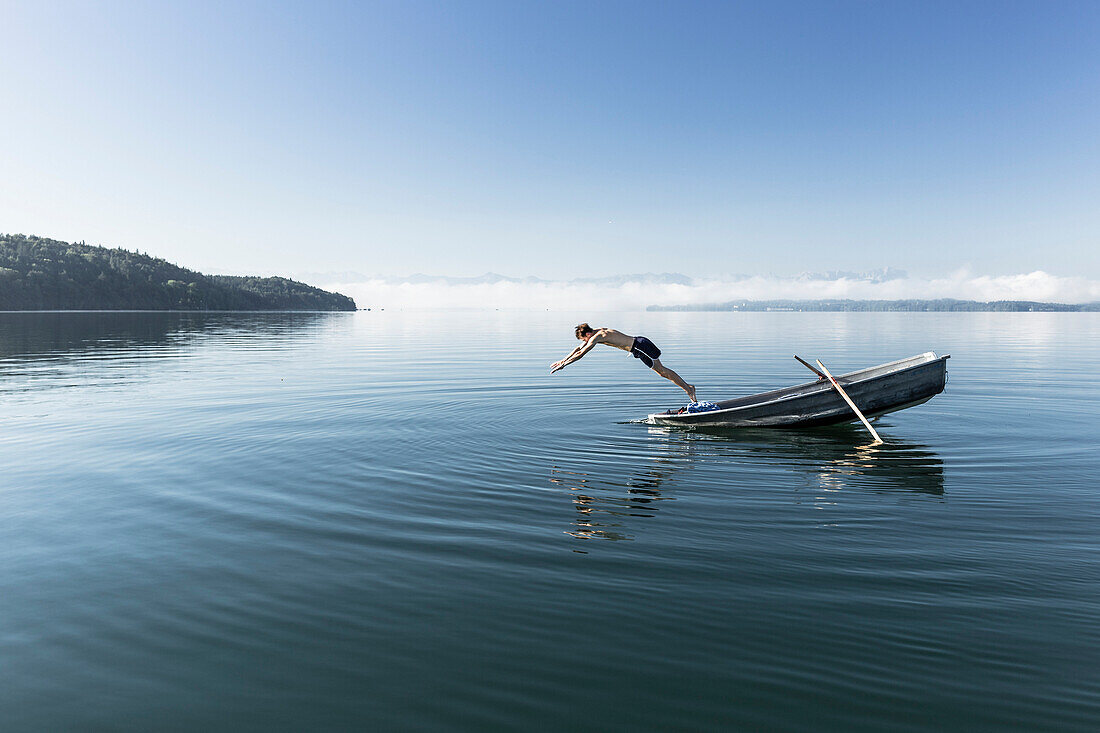 Man swimming in lake Starnberg, the Alps with mount Zugspitze in early morning fog, Berg, Upper Bavaria, Germany