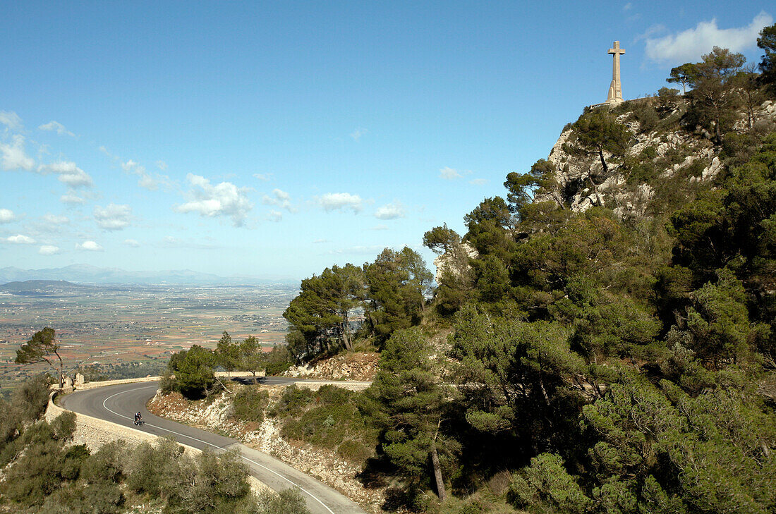 Cyclist on serpentine road with cross of Santuari de Sant Salvador Monastery, near Felanitx, Mallorca, Balearic Islands, Spain, Europe