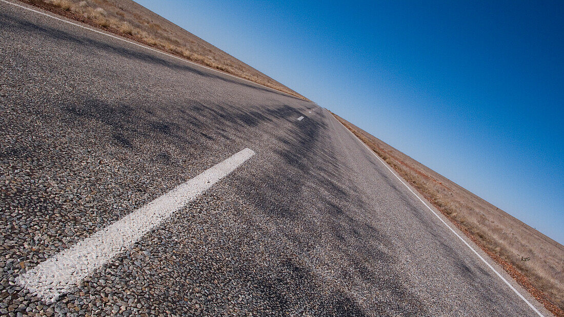 Schiefer Anblick einer langen geraden Straße durch das endlose Outback, Northern Territory, Australien