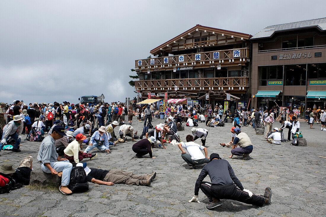 Menschen dehnen ihre Beine an der Basisstation um sich für den Aufstieg auf den Berg Fuji vorzubereiten, Mount Fuji, Region Chubu, Honshu, Japan