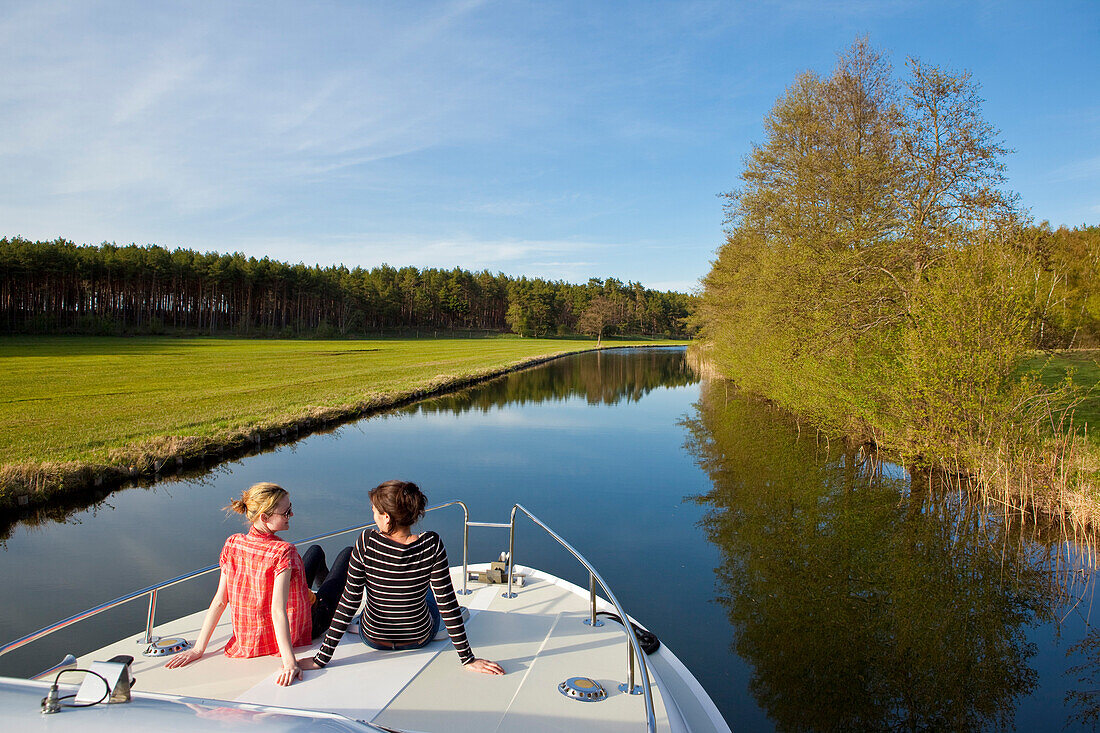 Two women relaxing and chatting on the bow of a houseboat, Grosser Zechliner See, North Brandenburg Seenplatte, Brandenburg, Germany