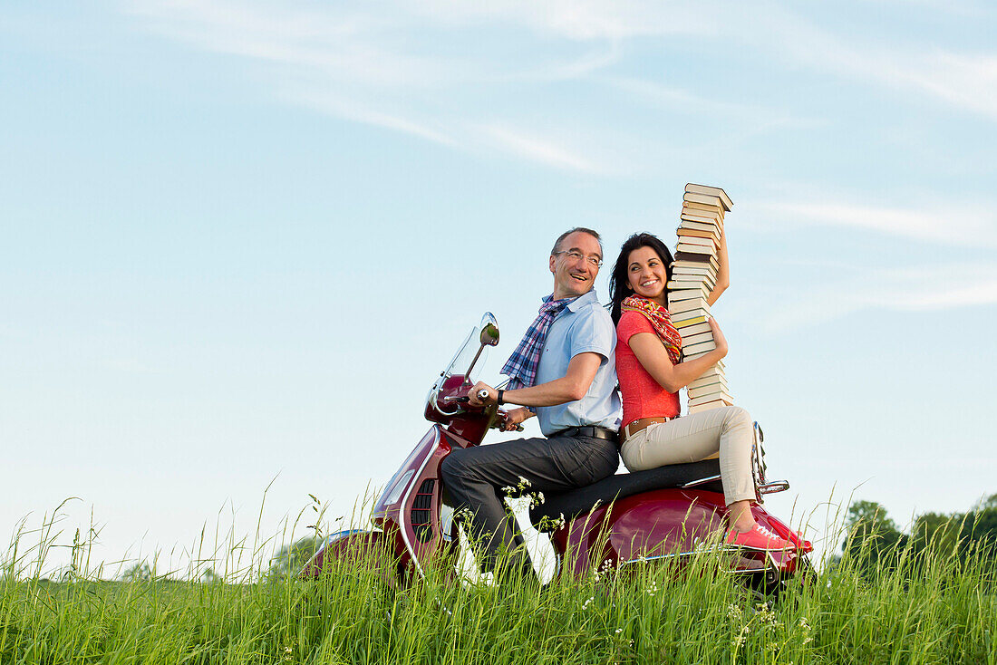 A man and a woman transporting a stack of books on a red Vespa scooter, Bad Wildungen, Hesse, Germany, Europe