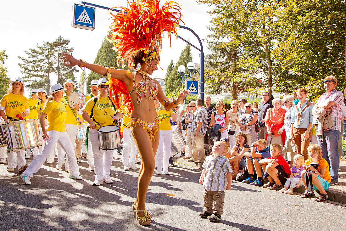 A young boy looking up to a beautiful female samba dancer wearing feather costume during the Samba Festival in Bad Wildungen, Bad Wildungen, Hesse, Germany, Europe