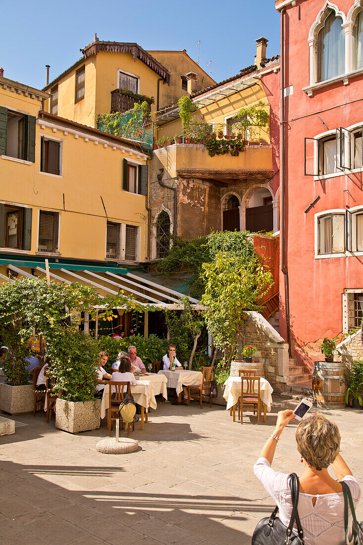 Eine Frau fotografiert Häuser und ein Café mit ihrem Smartphone, Venedig, Venetien, Italien, Europa