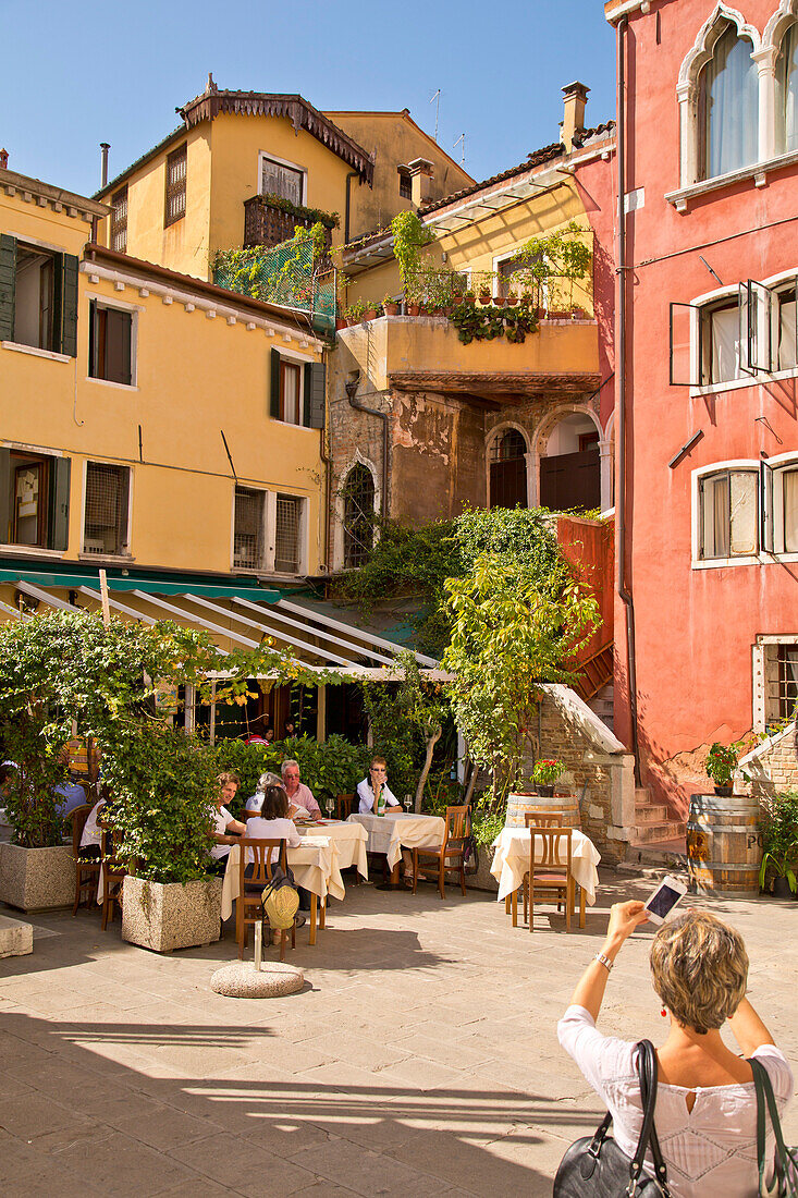 Woman taking a photograph of houses and a cafe with her smartphone, Venice, Veneto, Italy, Europe