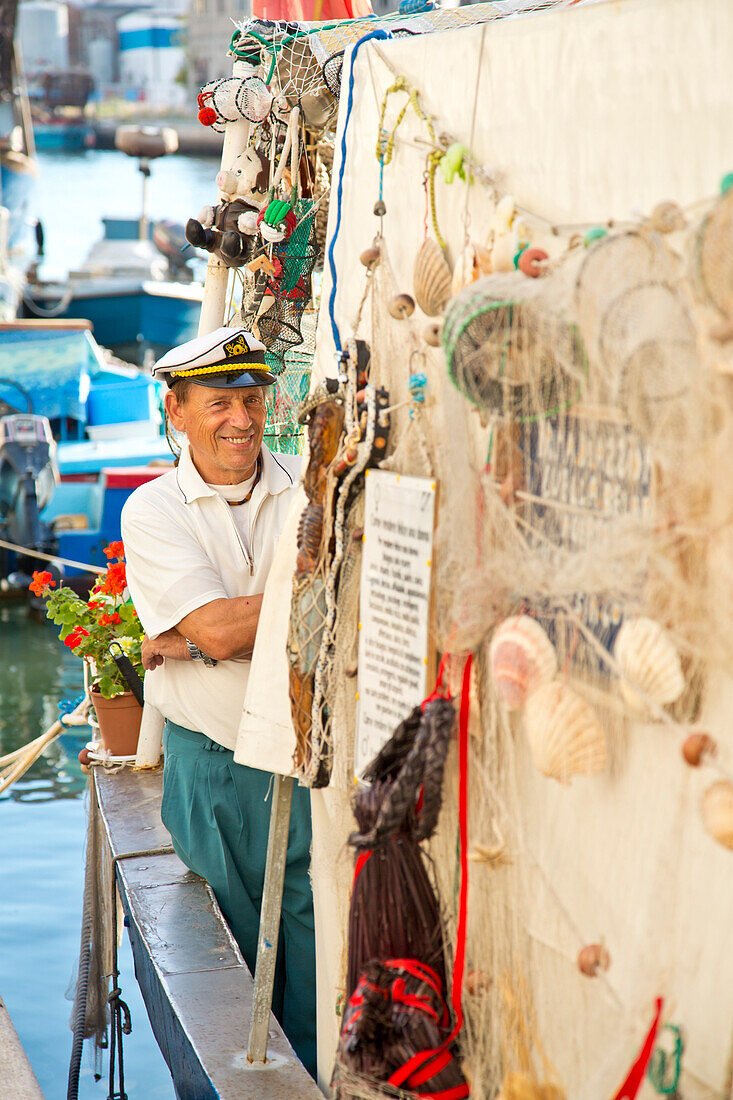 Freundlicher Mann mit Kapitänsmütze auf dem kunstvoll dekorierten ehemaligen Fischerboot Victoria, Chioggia, nahe Venedig, Venetien, Italien, Europa