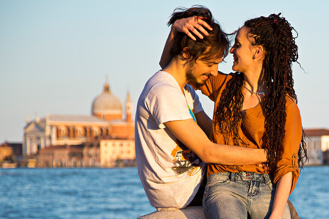 Young couple kissing on the banks of the Canale della Giudecca in Dorsoduro with Chiesa del Redentore church in the distance, Venice, Veneto, Italy, Europe