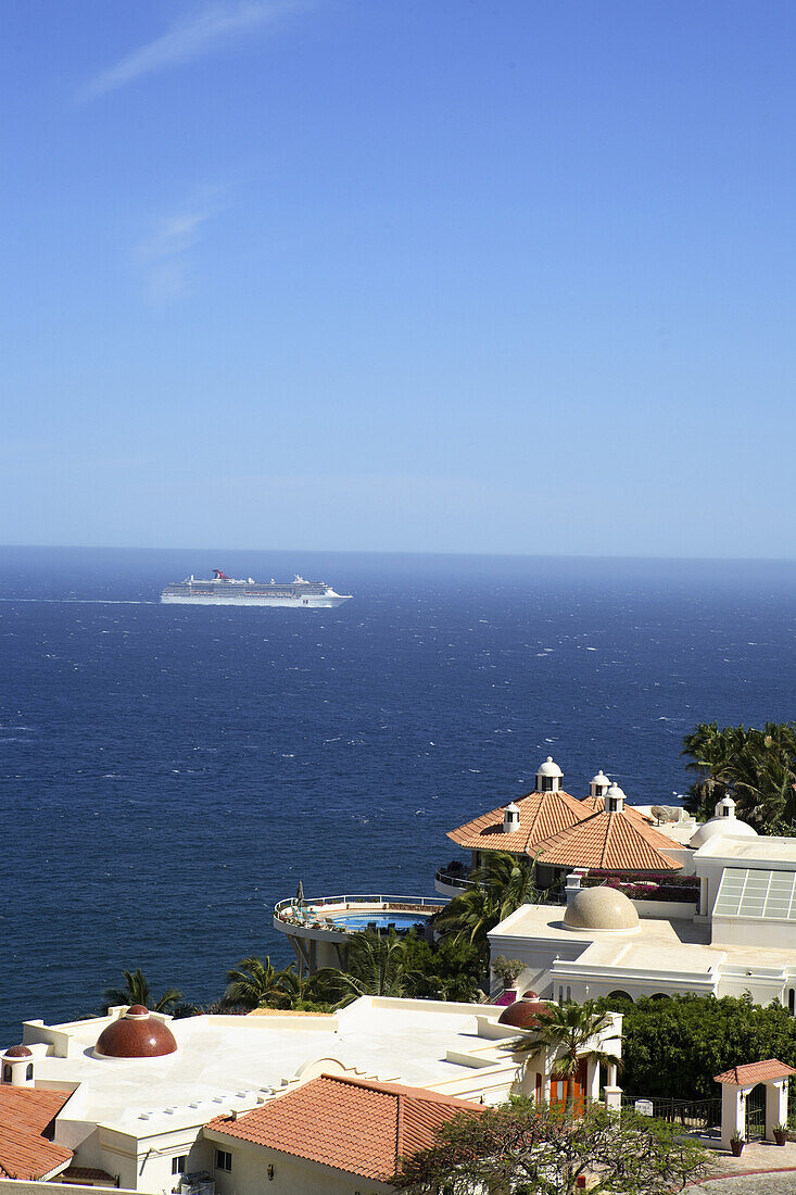 A large crusie ship sails past the exclusive multi-million dollar luxury villas that cling to the steep desert mountainsides in the Pedregal Hills overlooking the Pacific Ocean in Cabo San Lucas in Baja, Mexico. Photo by Harrison Shull/Aurora