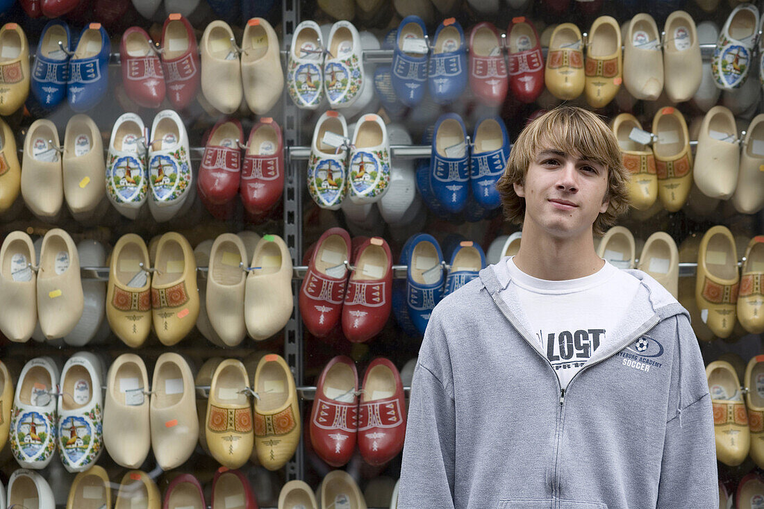 Young male tourist in Amsterdam, standing against a wall of clogs.