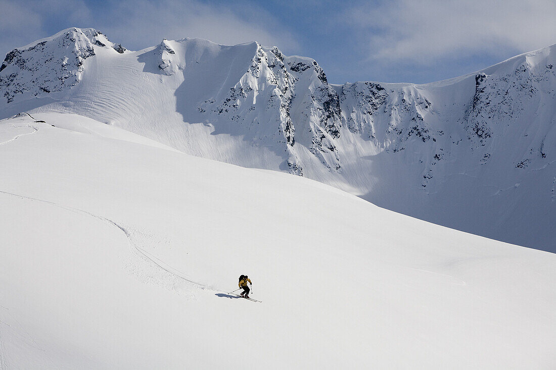 Man telemark skis on open slope in mountain backcountry near Haines, Alaska during heli skiing adventure.