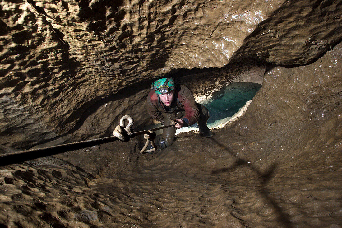 Rob Eavis ascends a knotted rope out above a pool of water in a cave in England called Streaks Pot.
