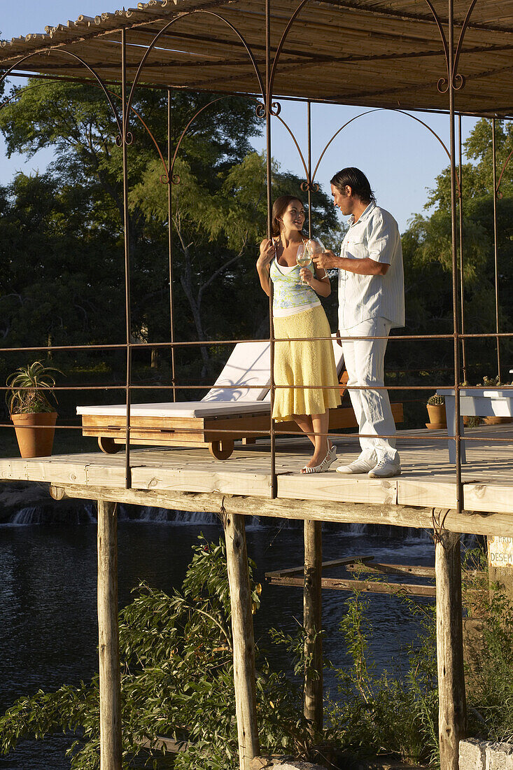 A young couple drinking wine on the deck overlooking a river in Carmelo, Uruguay.  releasecode: THS_0011, THS_0012