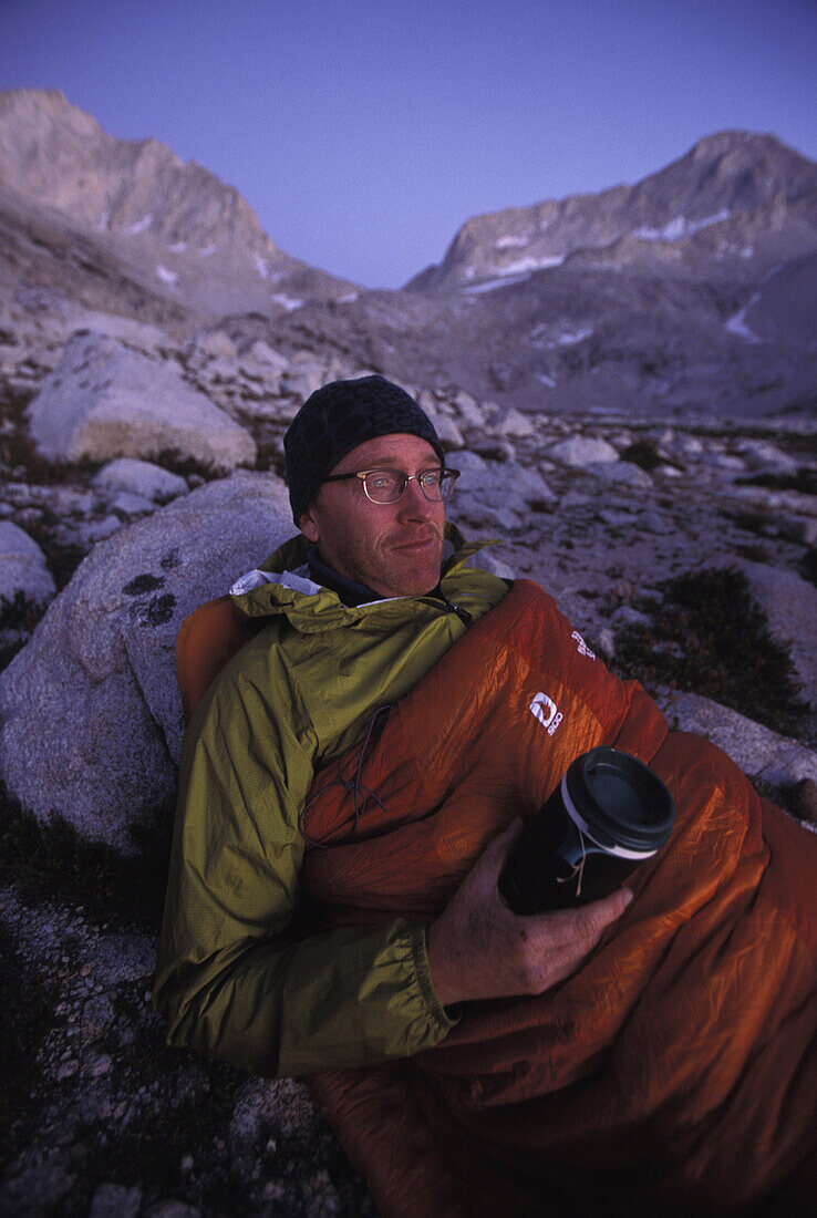 Dan Duane enjoying a hot drink in his sleeping bag while on a backpacking trip on the Sierra High Route, a 195 mile trackless path almost entirely between 9,000 and 11,500 feet in elevation in the Eastern Sierra Nevada mountains in California.
