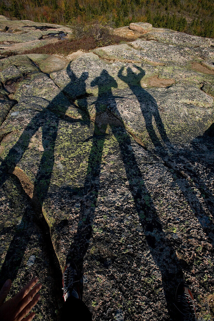 Three friends make shadow art on the granite top of  Cadillac Mountain in Acadia National Park, Maine.