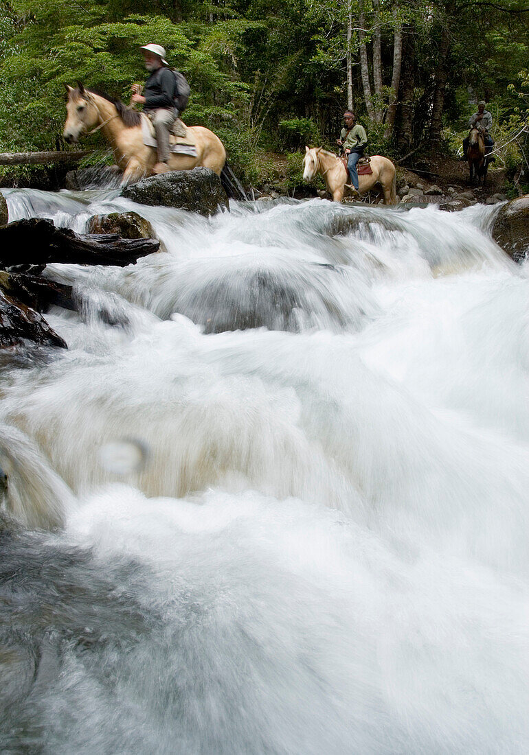 Omer Thompson, John Lockwood, and Chris Spelius cross a river by horseback during a wilderness adventure in Futaleufu, Chile.
