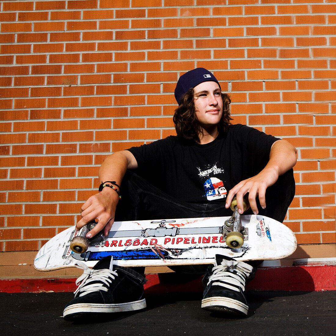 High school aged skateboarder sitting on a curb, Oceanside, California.