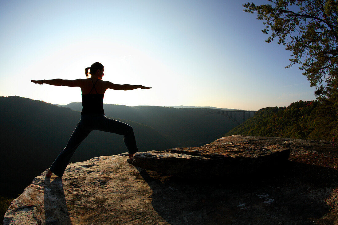 Sarah Chouinard enjoys a late afternoon yoga session pose : Warrior II - virabhadrasana, atop the Bosnian Buttress along the rim of the New River Gorge near Fayetteville, WV