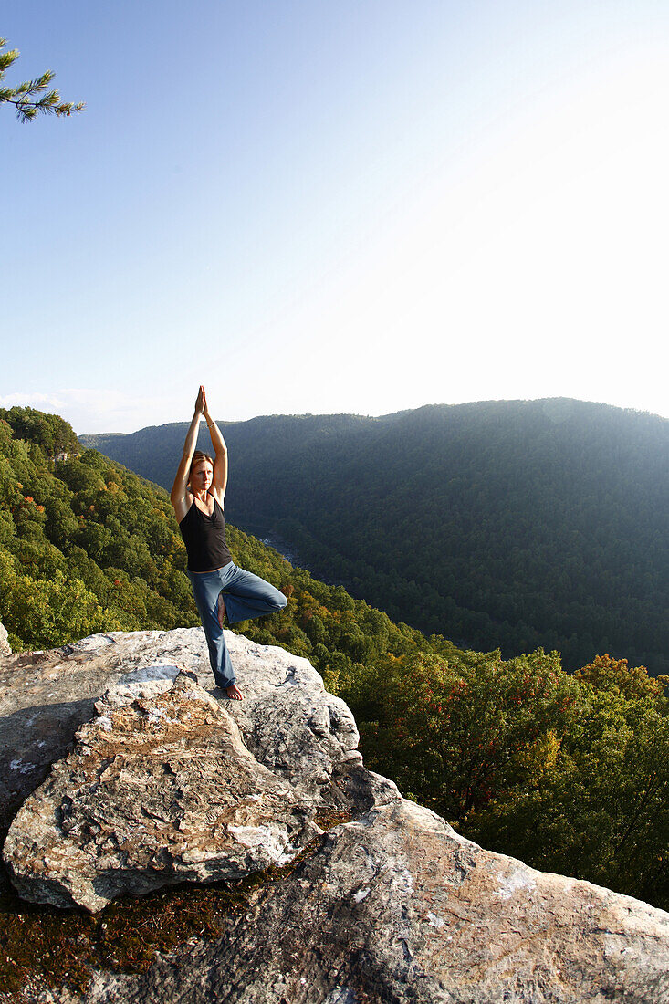 Sarah Chouinard holds a late afternoon yoga session pose : Tree - vriksha asana, atop the Bosnian Buttress along the rim of the New River Gorge near Fayetteville, WV