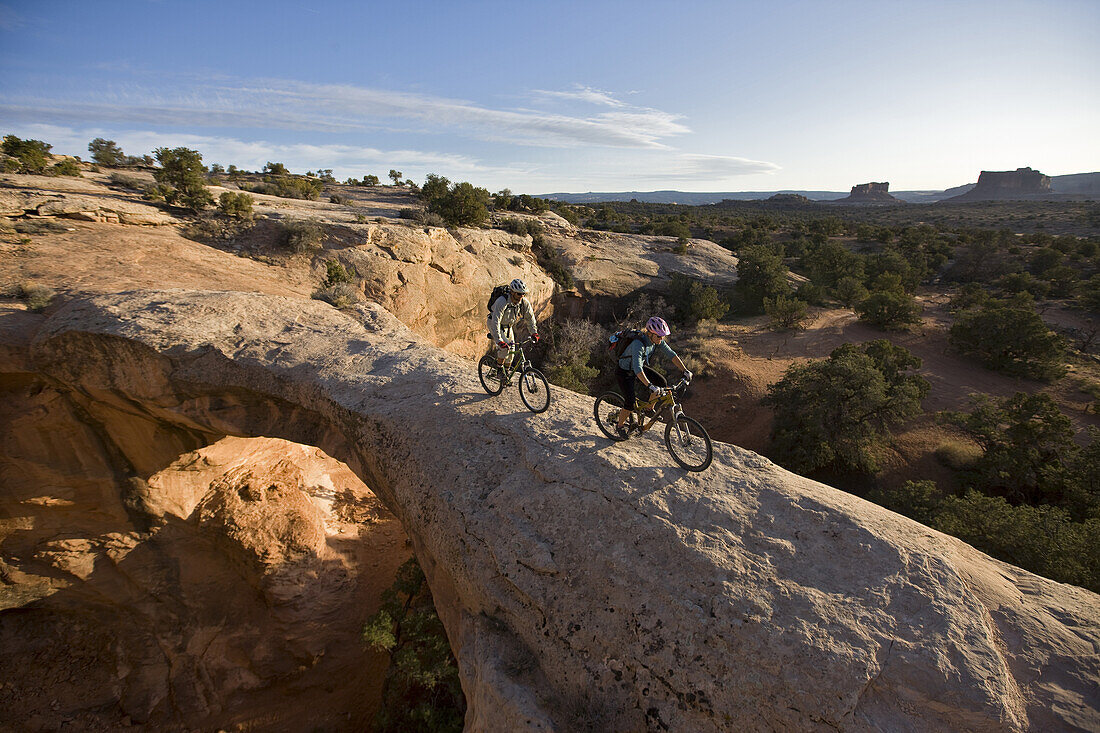Jess Reilly and Mark Howe mountain biking across an arch near Moab, Utah.
