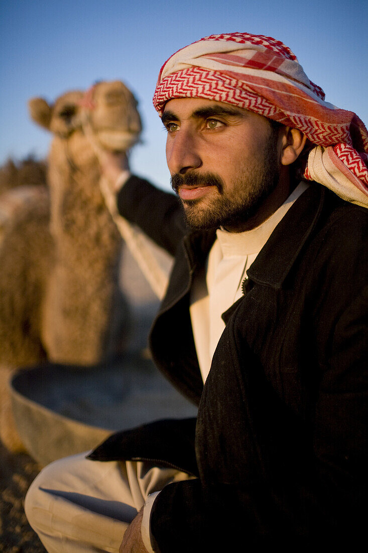 Palmyra, Syria - January, 2008: Portrait of a young Syrian Bedouin  man with his camel in the desert.