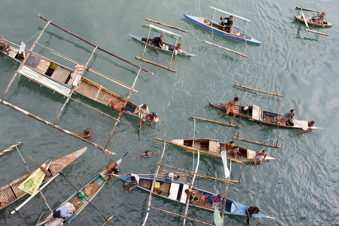 'Filipinos in small banca boats chase Super Ferry in hopes for coins thrown from passengers in the upper decks of the ocean liner; Cebu, Philippines.'