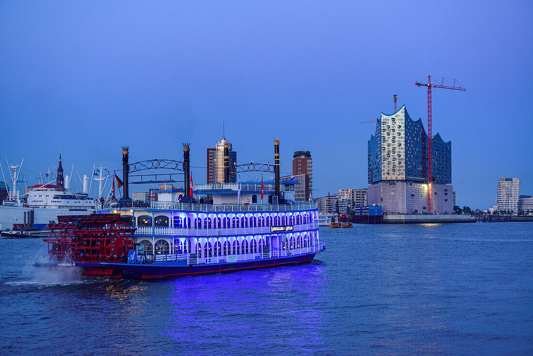 Illuminated paddle ship Louisiana Star sailing on the river Elbe towards Kehrwiederspitze and Elbphilharmonie, Hamburg, Germany