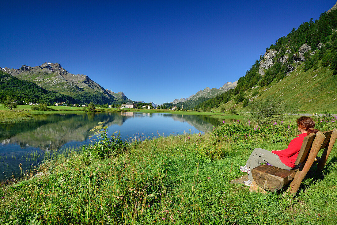 Frau sitzt auf einer Bank mit Blick über den Inn auf Sils-Baselgia, Sils, Oberengadin, Engadin, Graubünden, Schweiz