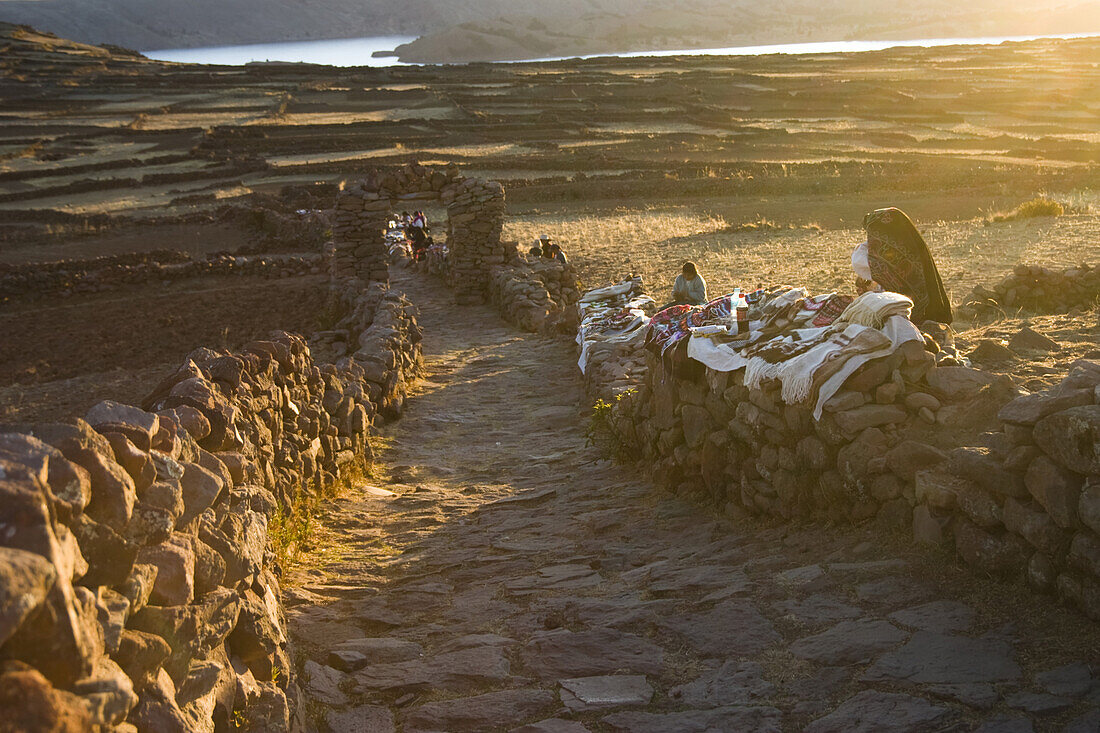 Local women display their textile handicrafts for sale along the stone path at the summit of Taquile Island on Lake Titicaca, Peru.