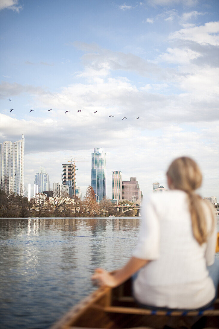 A flock of birds pass in front of a female paddler on Lady Bird Lake in downtown Austin, TX. Canoeing on the lake is a popular recreational activity in Austin.