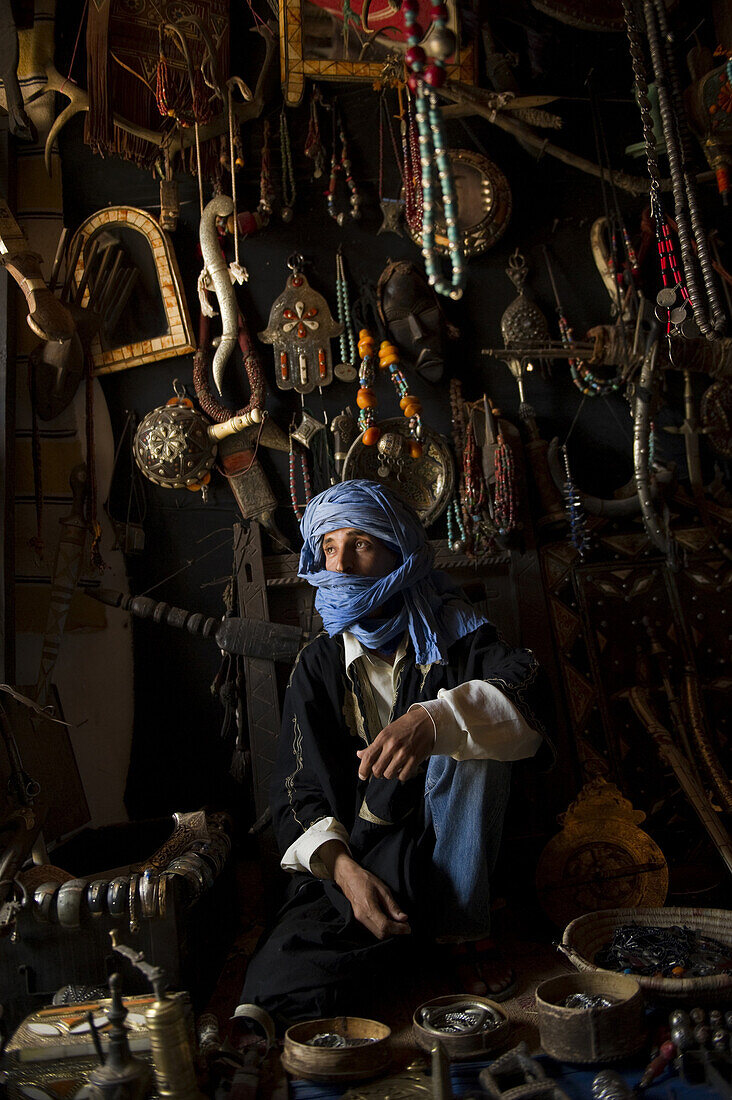 A young man sits on the floor of his store surrounded by his beads, mirrors, knives and silver which he sells to passing tourists in Morocco.