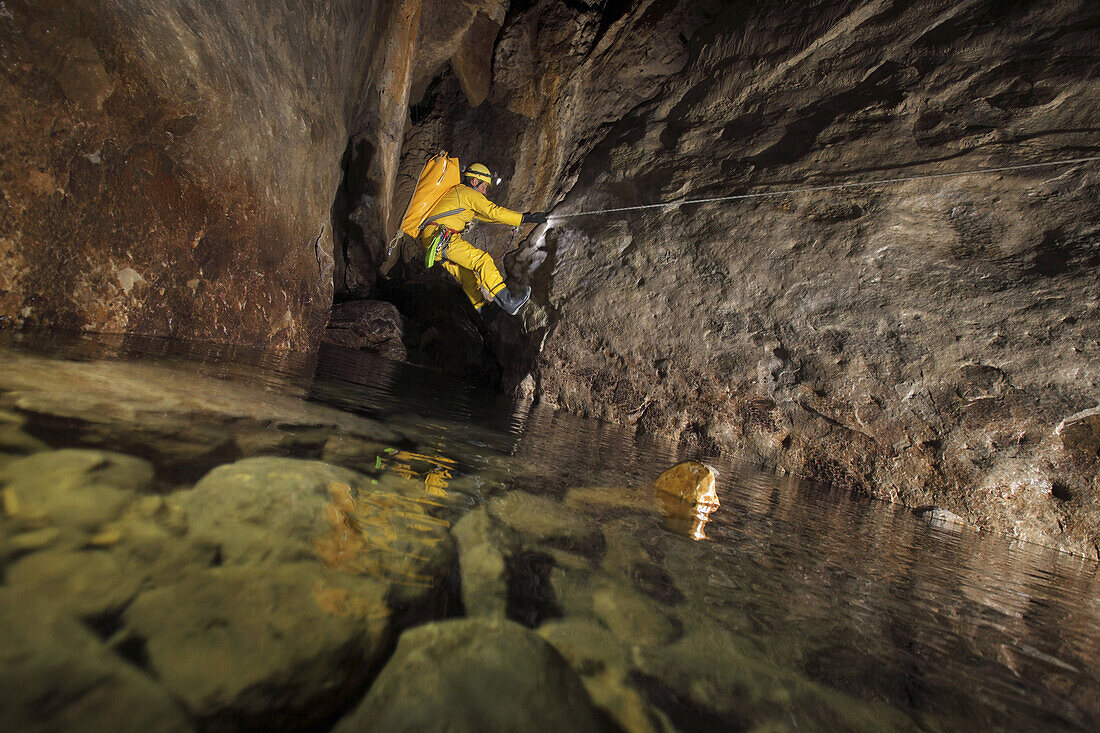 British male cave explorer tackles a tensioned rope line climb to keep him away from the water in a cascade, part of the classic famous cave in France called The Gouffre Berger high in the Vercors region.