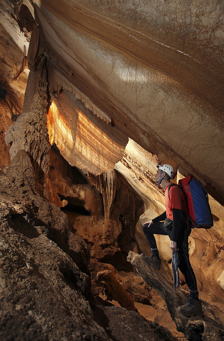 A male cave explorer admires a giant curtain formation made out of crystal calcite, deep underground in Racer Cave, Gunung Mulu National Park, Sarawak, Borneo.