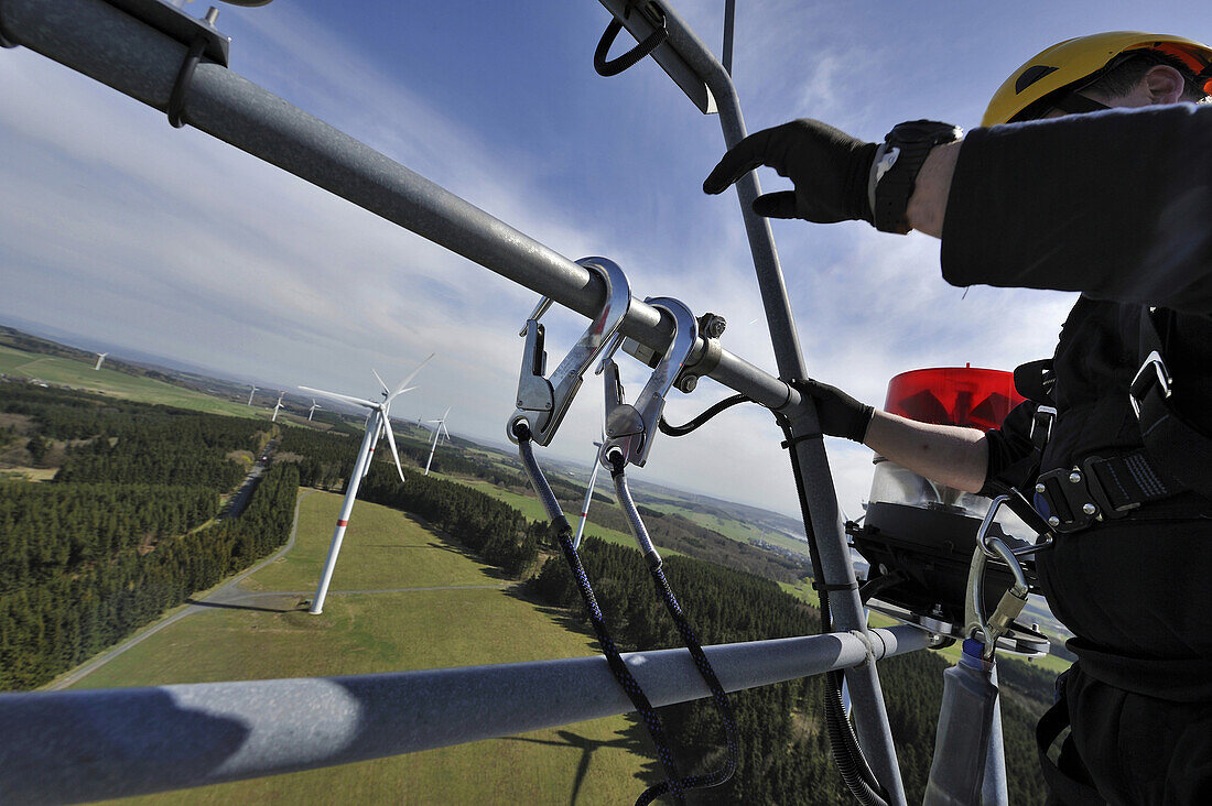 A technician carefully attaches fall protection safety equipment to an anchor on top of the nacelle of a wind turbine in Germany.