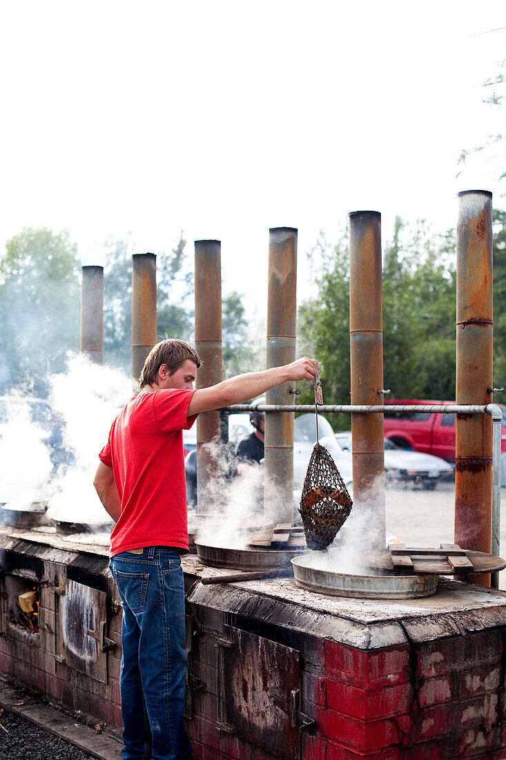 MAINE, USA. A man lifts a bag of cooked lobsters out of an outdoor oven at a restaurant.