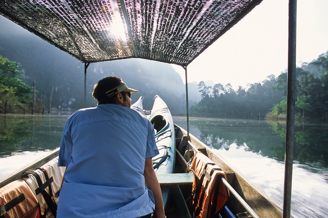 A young man rides a longtail boat shuttle across Chiaw Lan Lake in Khao Sok National Park, Thailand.