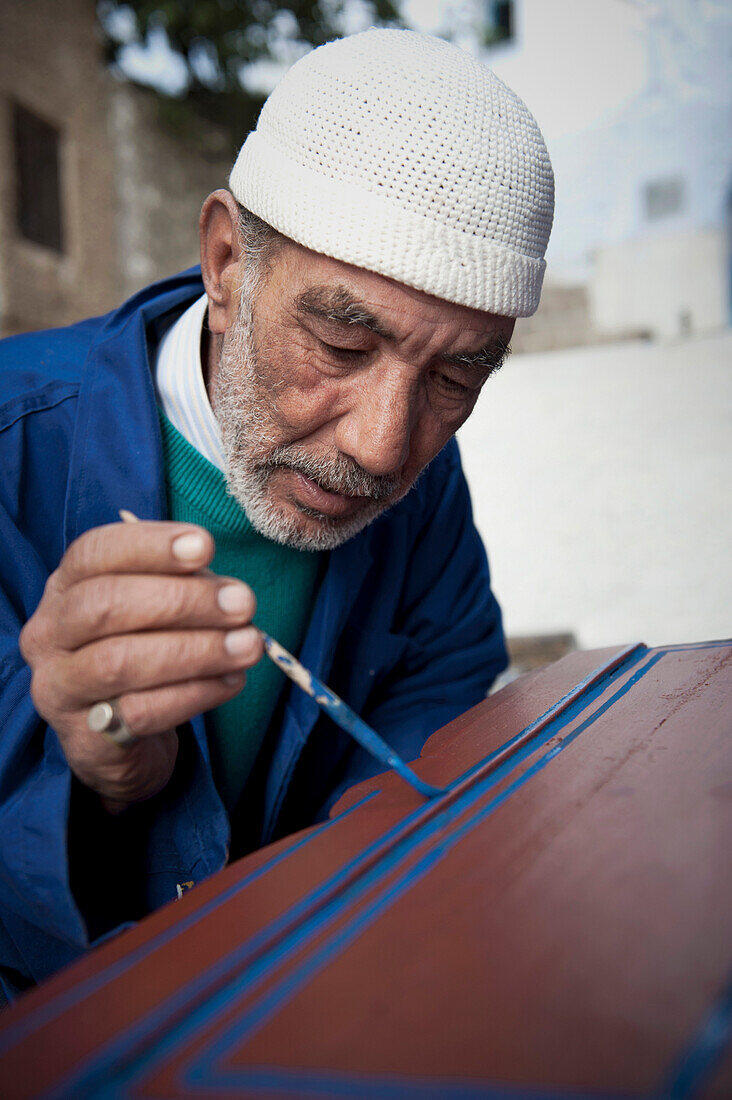 Portrait of a senior man hand painting one of his handmade crafts, Chefchaouen, Morocco