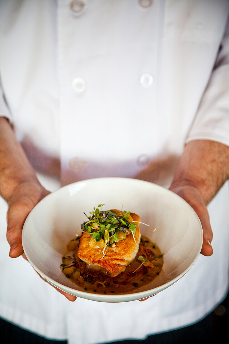CHARLOTTE, NORTH CAROLINA, USA. A chef holds a bowl of flounder. root vegetable cake, almonds, golden raisins & curry beurre blanc at a restaurant called Good Food on Montford.