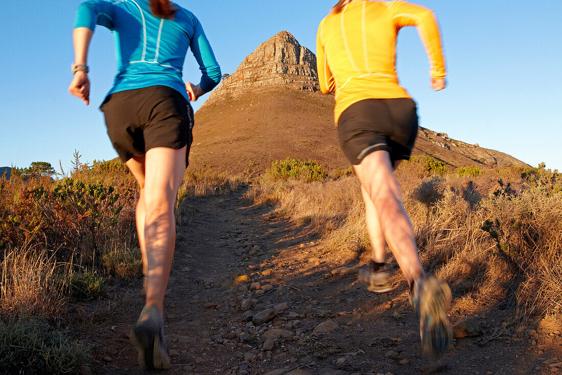 Katrin Schneider and Susann Scheller running on the trail between Signal Hill and Lion's Head above the city of Cape Town just after sunrise. Cape Town, South Africa.