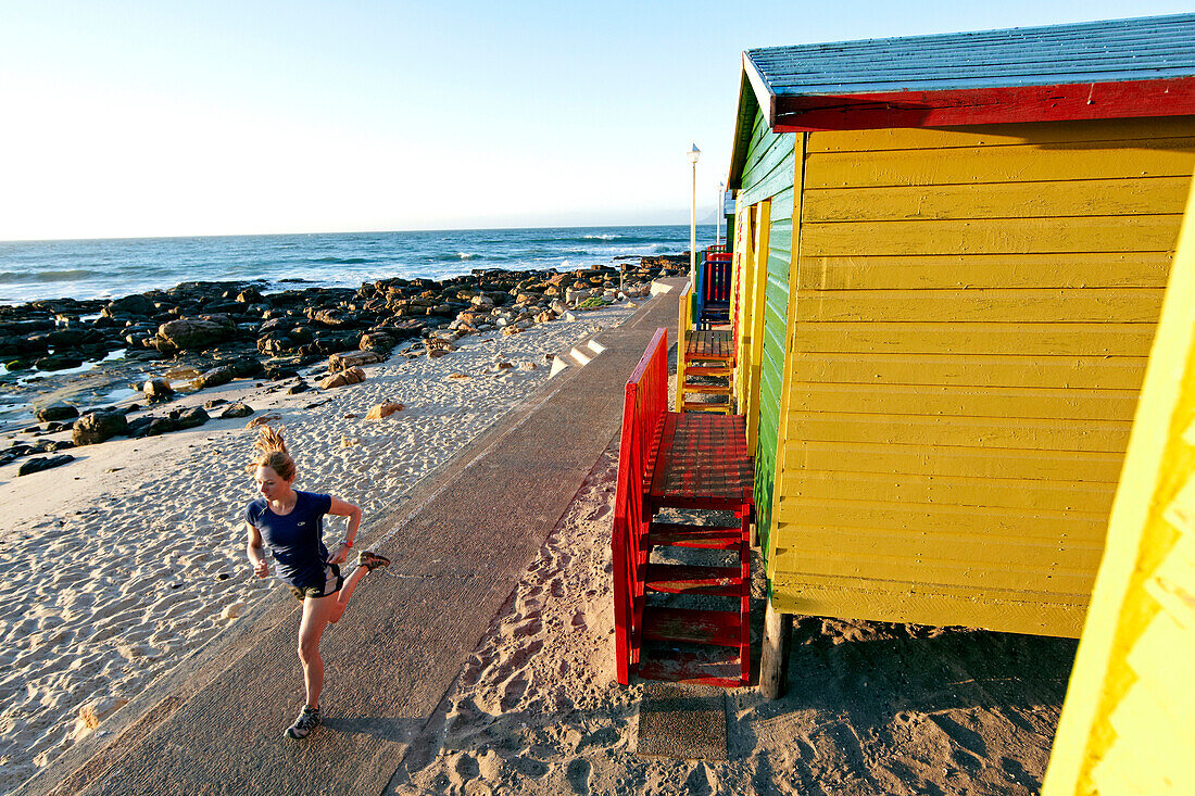 Katrin Schneider running past the famous and colorful bathing huts in St.James near Muizenberg. Cape Town, South Africa.
