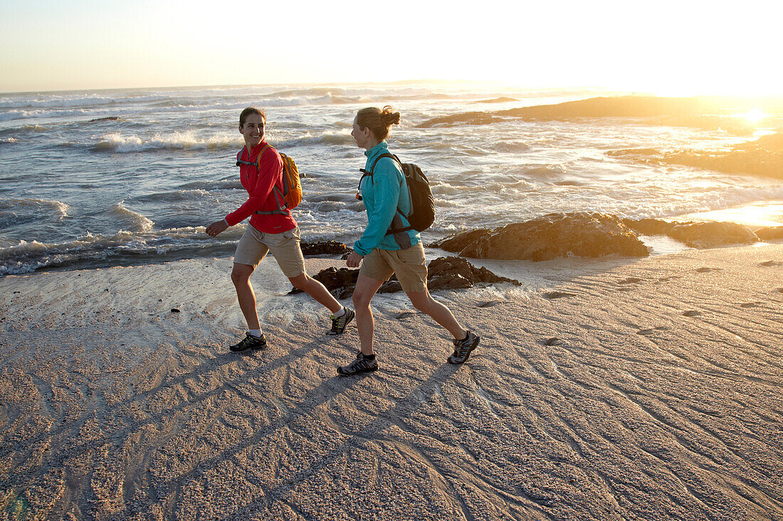 Katrin Schneider and Susann Scheller hiking along Bloubergstrand beach in Cape Town at sunset. Cape Town, South Africa.