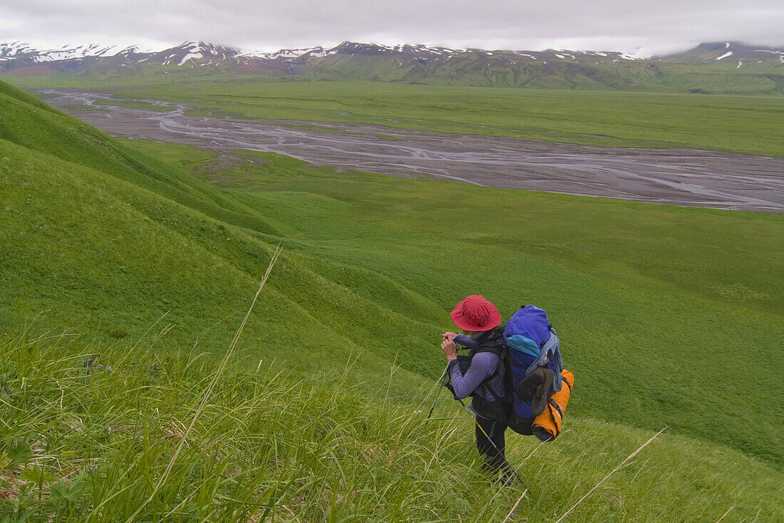 A woman hiking up a ridge above a river on Umnak Island in the Aleutian Islands.