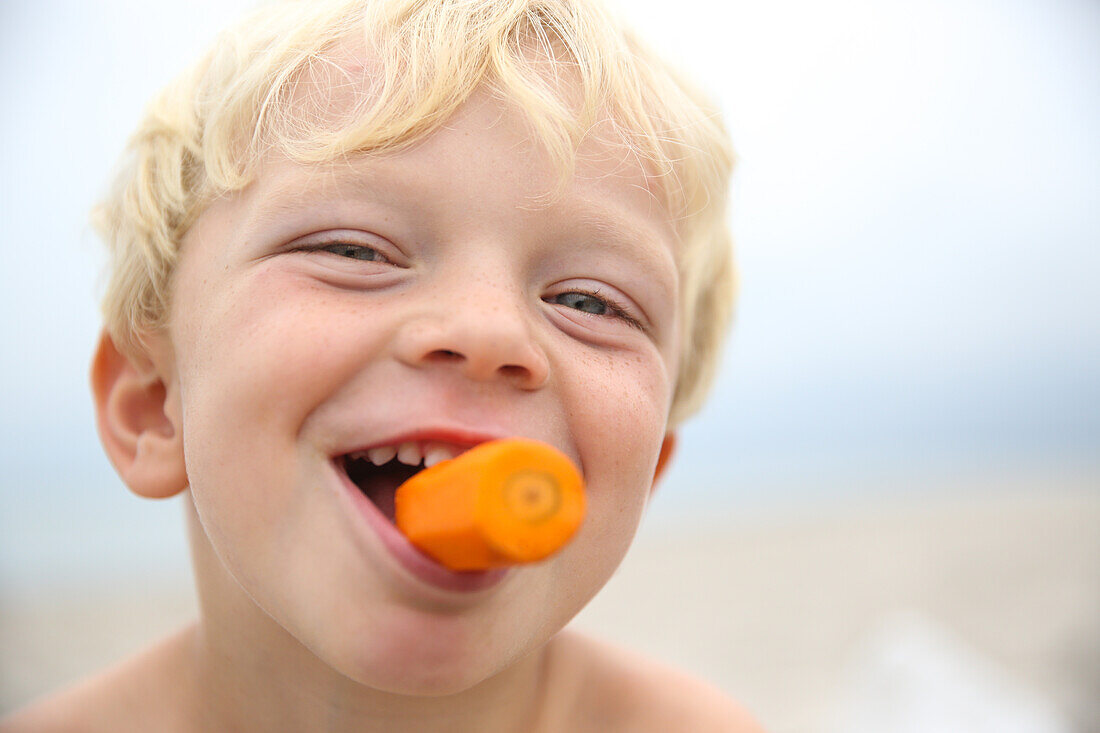 Junge (4 Jahre) mit einer Möhre im Mund, Marielyst, Falster, Dänemark