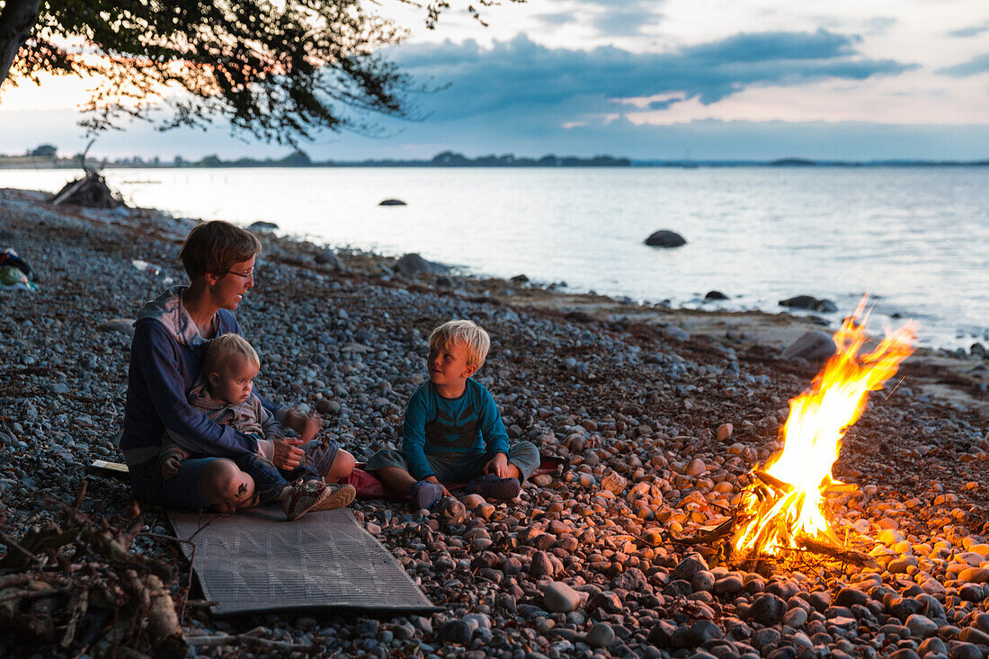 Mother and children (1-4 years) sitting around a campfire, Naesgaard, Falster, Denmark