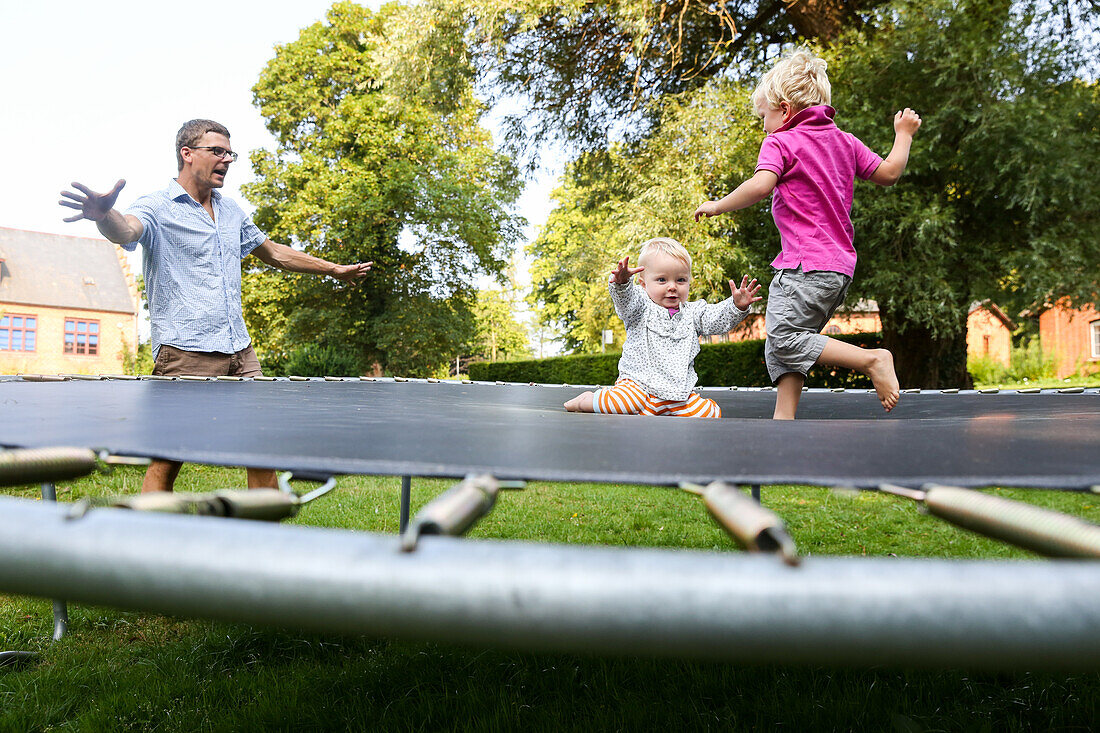 Vater spielt mit seinen zwei Kindern (1-4 Jahre) auf einem Trampolin, Stege, Insel Mön, Dänemark