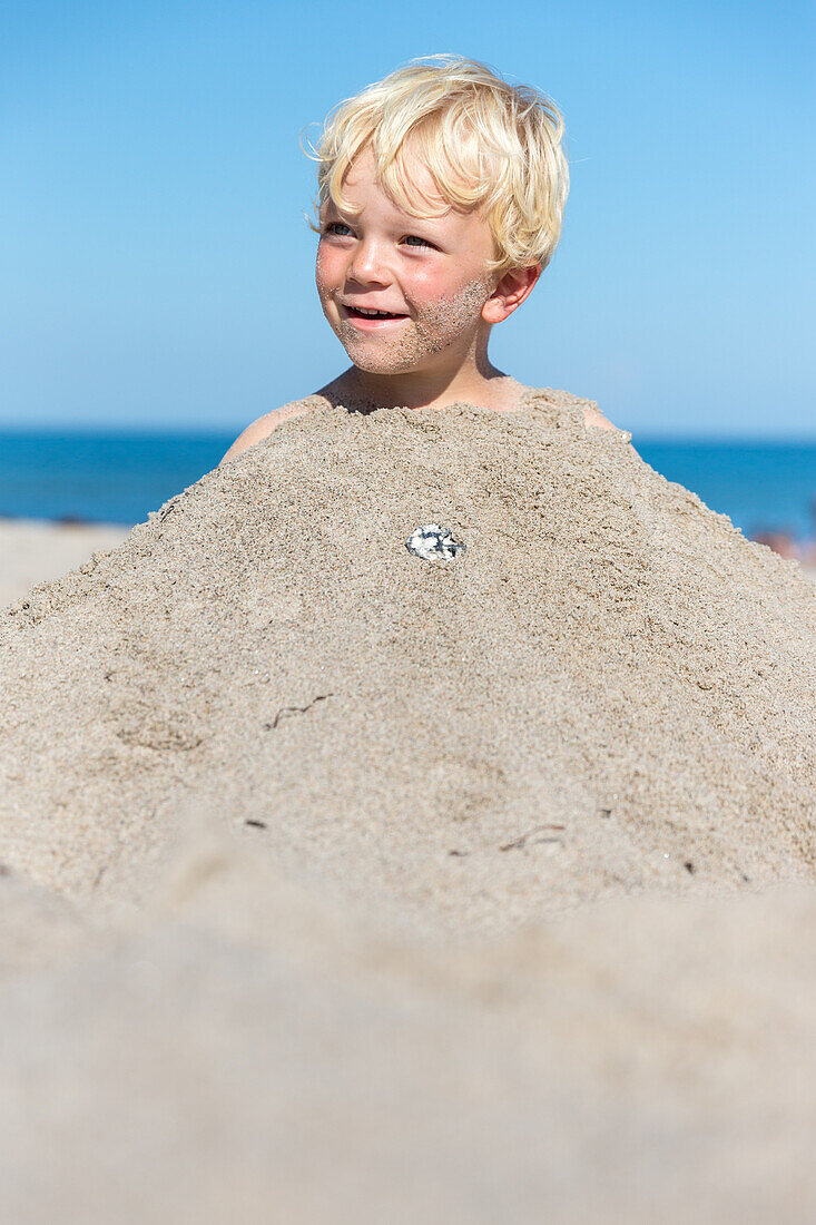Boy (4 years) buried in mound of sand, Marielyst, Falster, Denmark