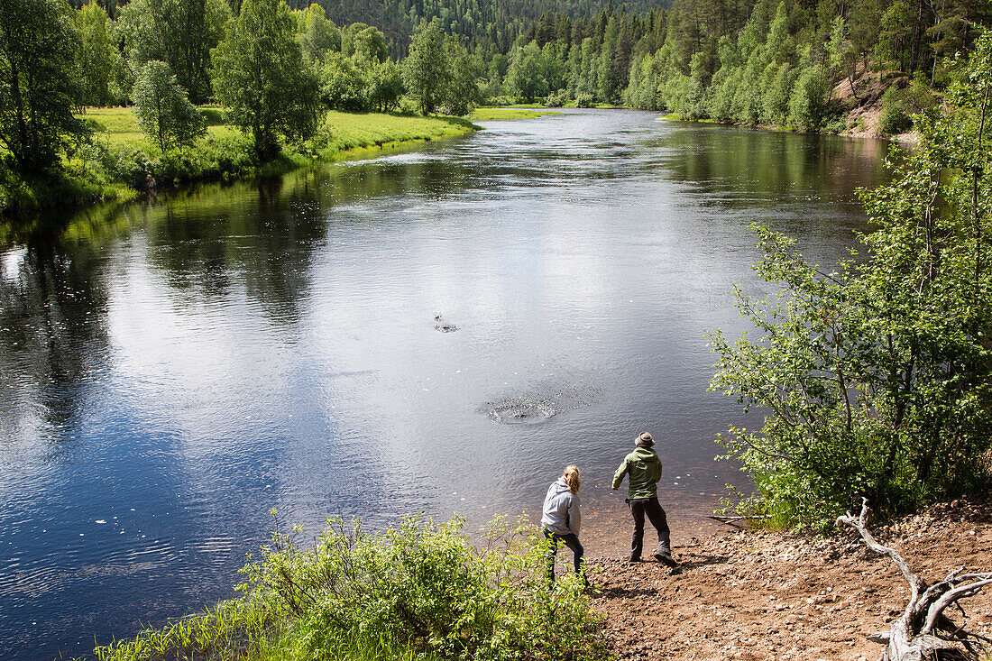 Zwei Personen lassen Steine am Fluss Oulankajoki springen, Nationalpark Oulanka, Nordösterbotten, Finnland
