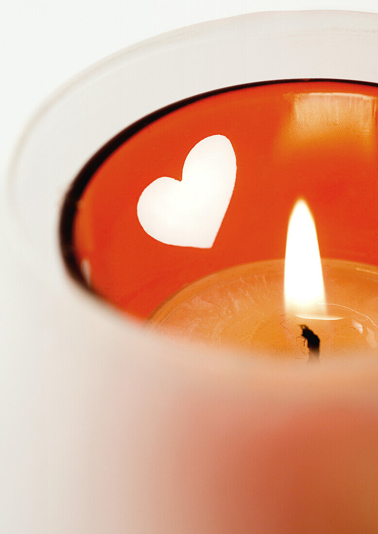 Lit candle in candleholder with heart pattern