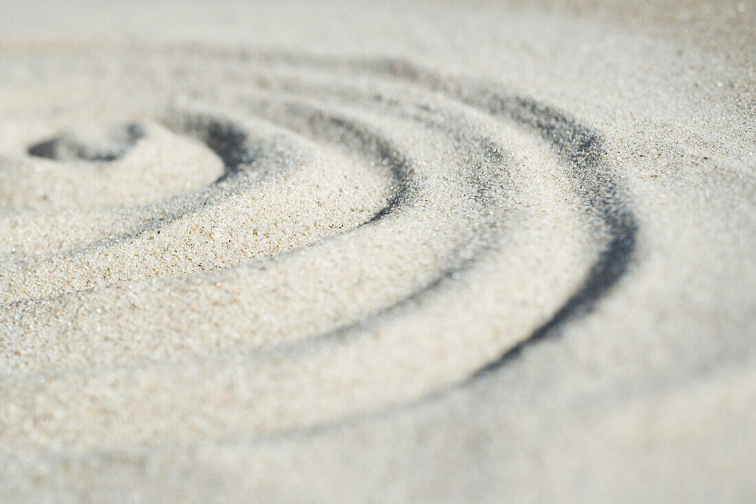 Spiral shape drawn in sand, close-up, surface level